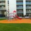 Mustekala leikkikenttä kaupunkialueella, punainen liukumäki ja oranssi kumipäällyste.