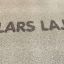 Kumiset laatat Rubber Tiles 55 tekstillä LARS LAJ painettuna harmaalla pinnalla.